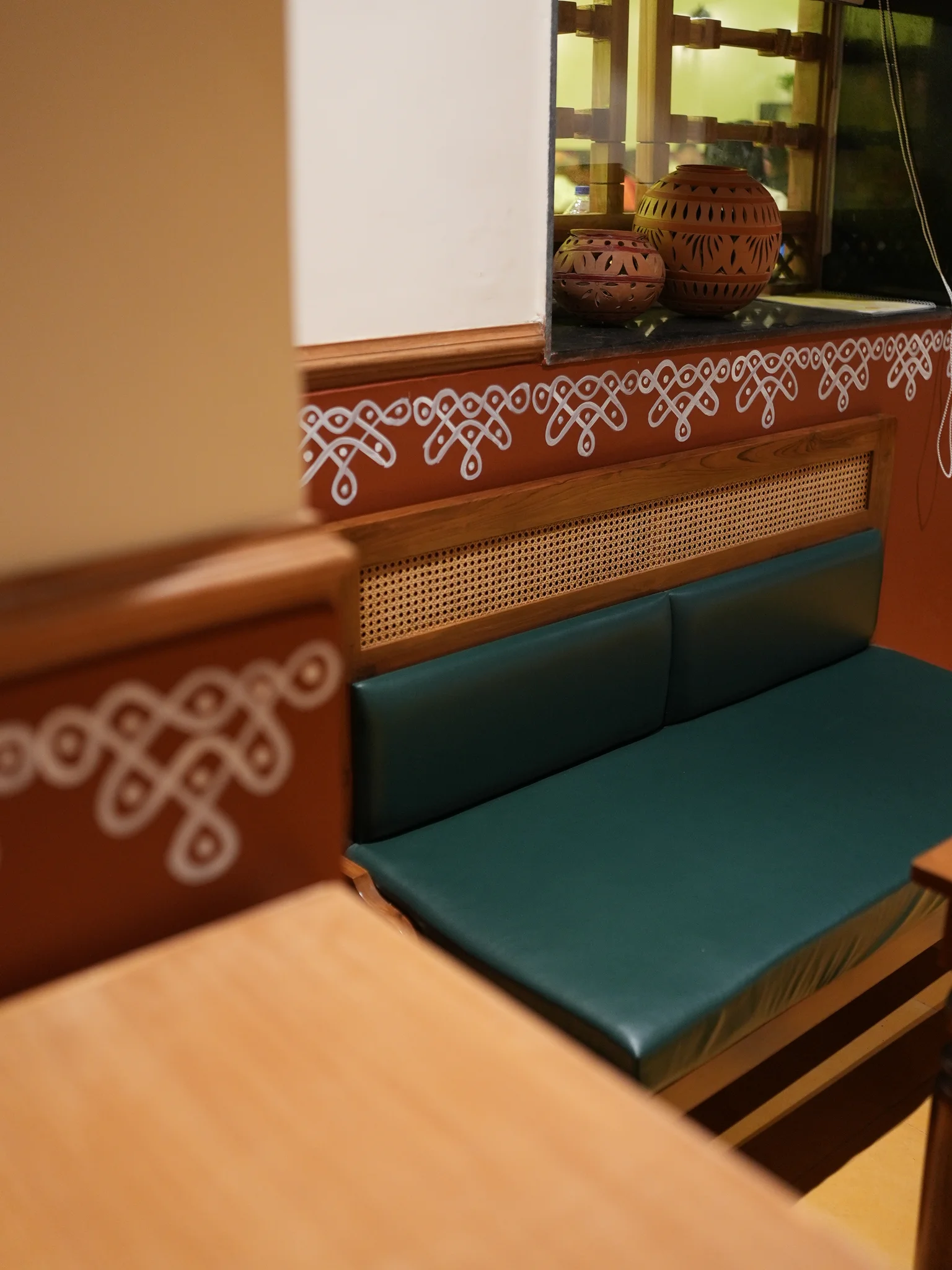 Warm terracotta walls with Indian decorative motifs, clay pots, and teal upholstered seating