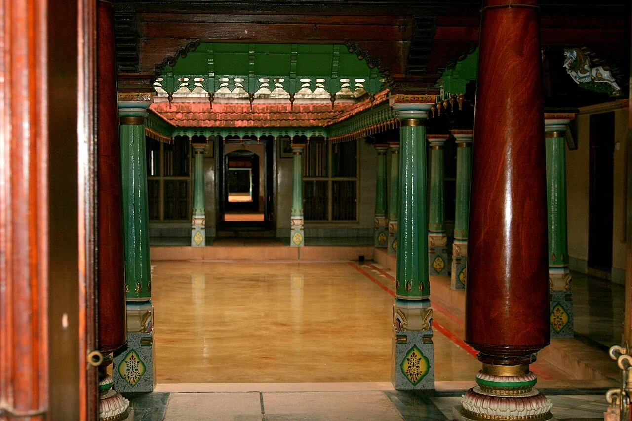A Chettinad house courtyard framed by painted timber columns, deep thresholds, clay roof tiles, and a sequence of shaded rooms