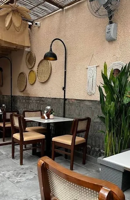 Beanery Café table beside plants, woven wall baskets and a black wall lamp.