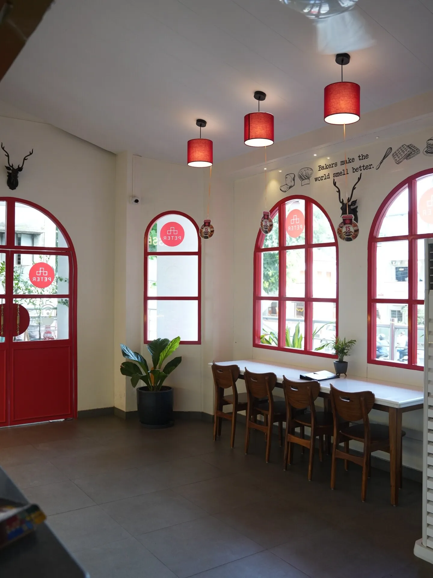 Café Peter Erandwane Pune interior — red-framed arched windows, warm pendant lighting, and compact dining seating. Interior design by prāngaṇa.