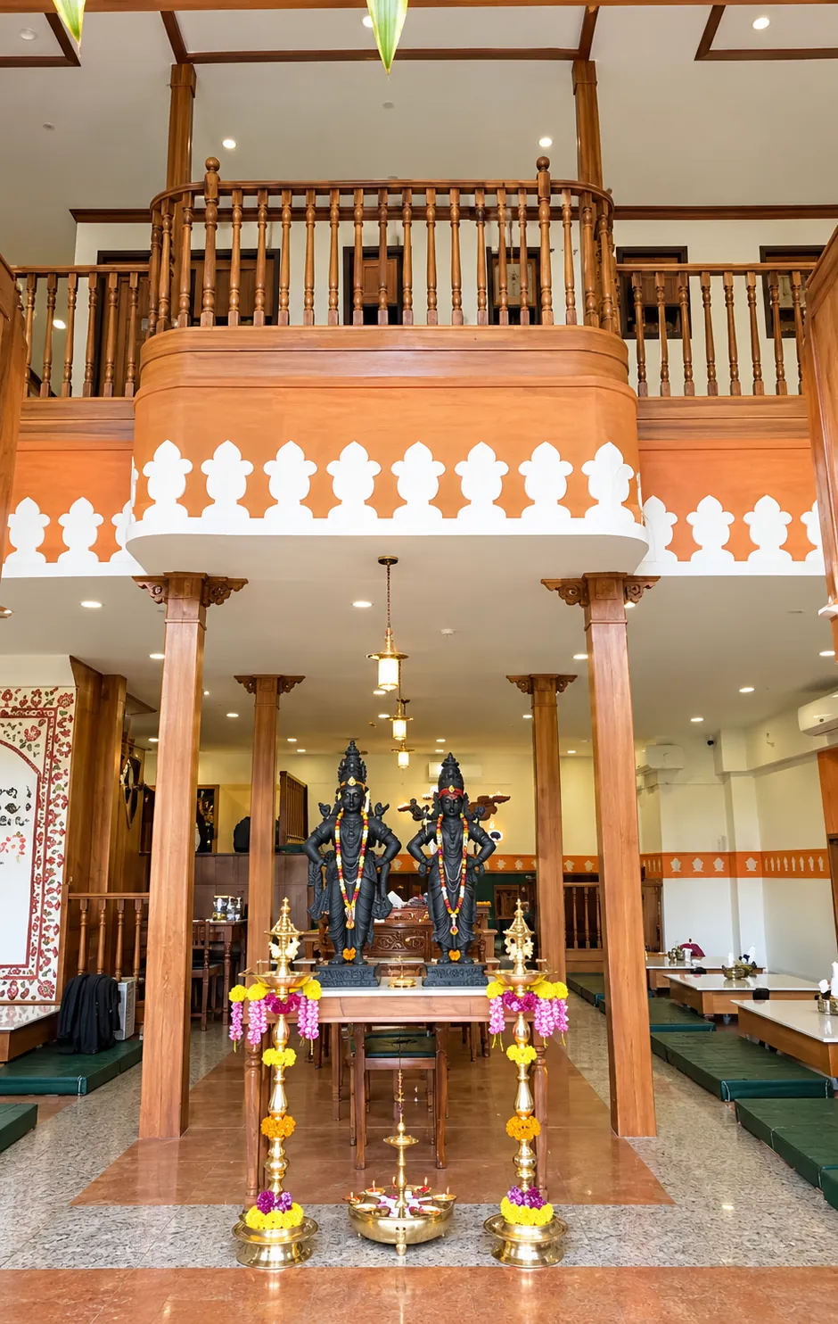 Double-height Purnabramha dining interior with a central garlanded display, timber columns and an upper railing.