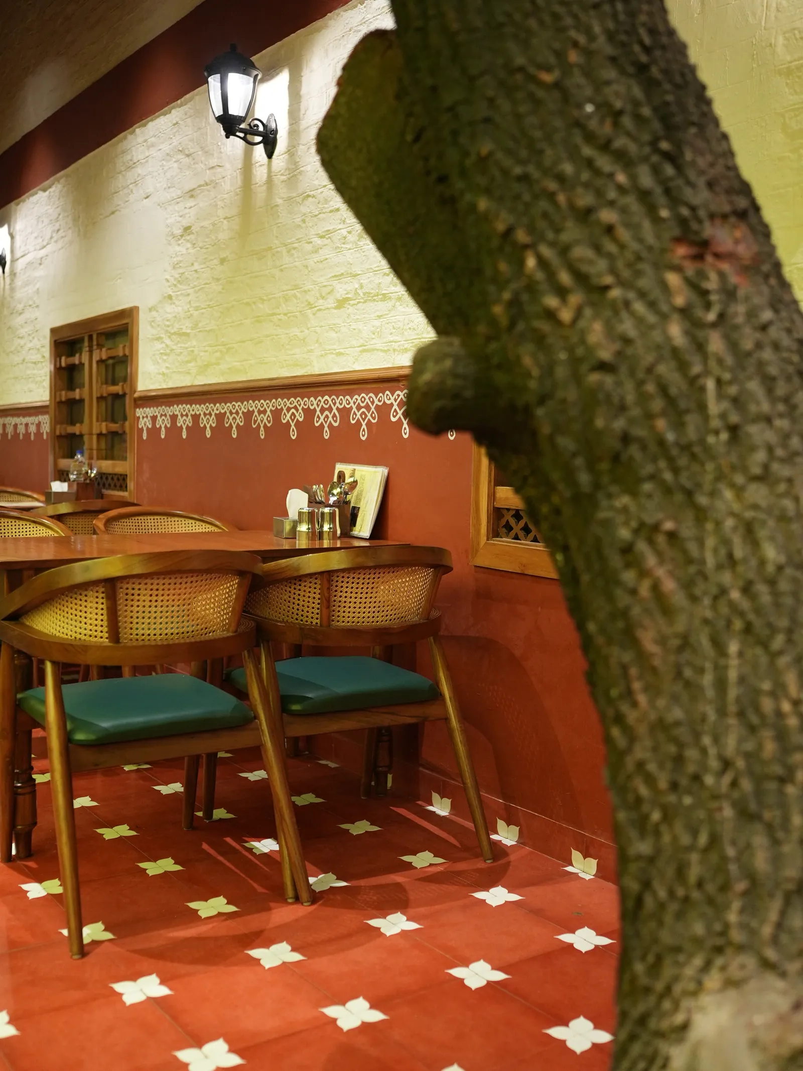 Dining tables and chairs beside a tree trunk at Secret Sambar, with a red-and-white patterned floor.