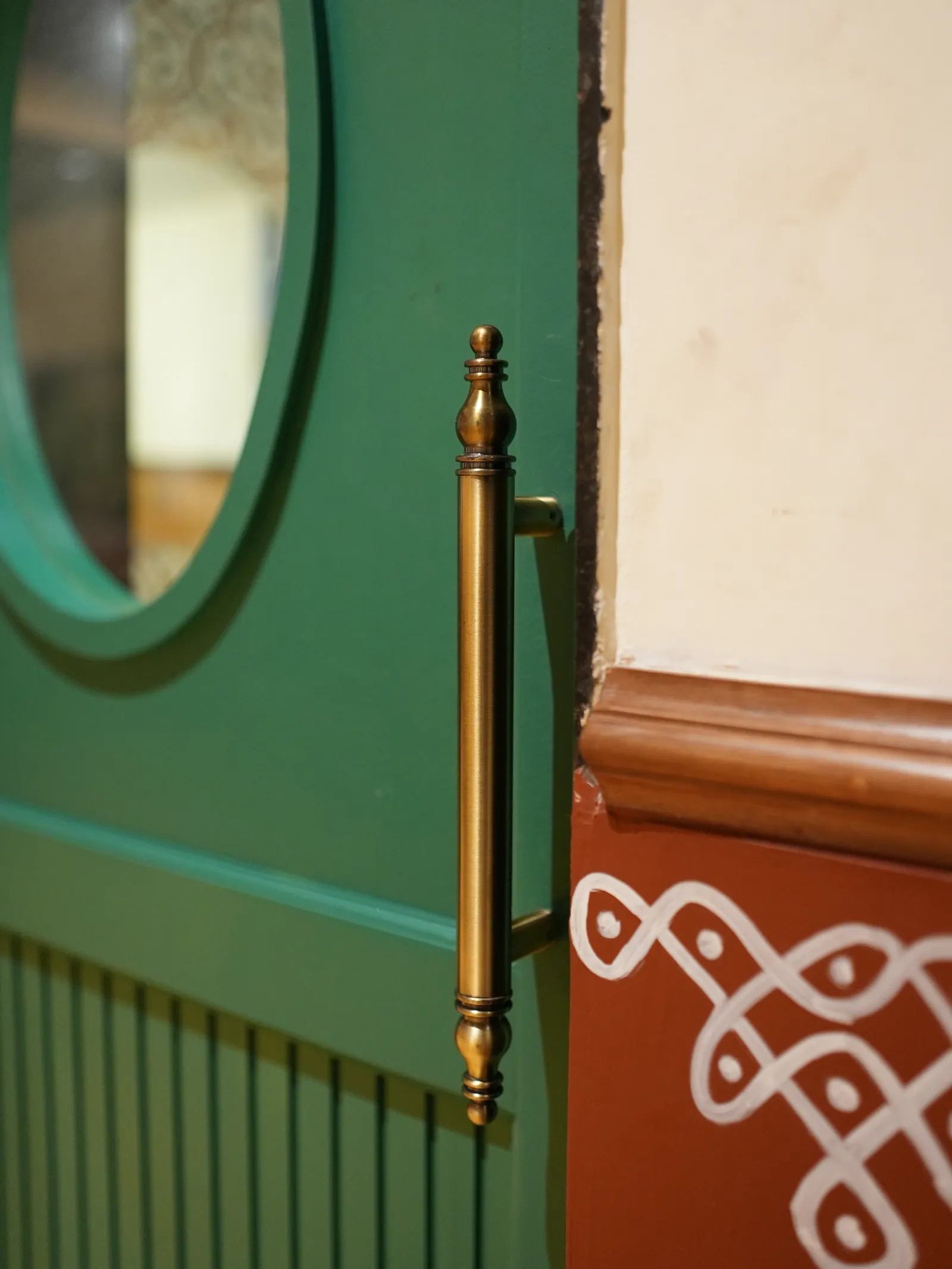 Green door with a vertical metal handle beside a white pattern on a red wall at Secret Sambar.