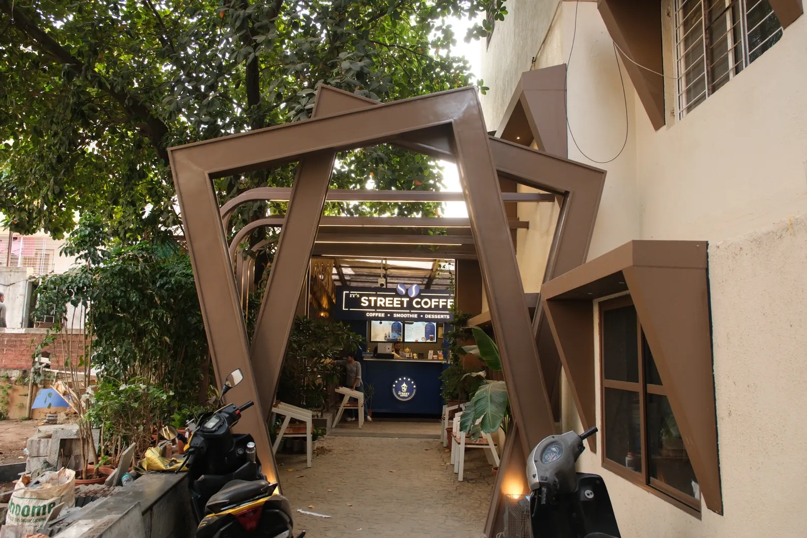 Street Coffee BVP Pune — framed exterior approach with trees and cafe frontage. Interior design by prāngaṇa.
