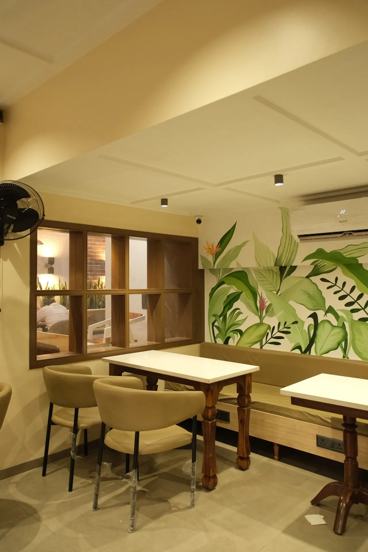 Seating bay at Street Coffee BVP Pune with botanical mural, shelving, and cafe tables.