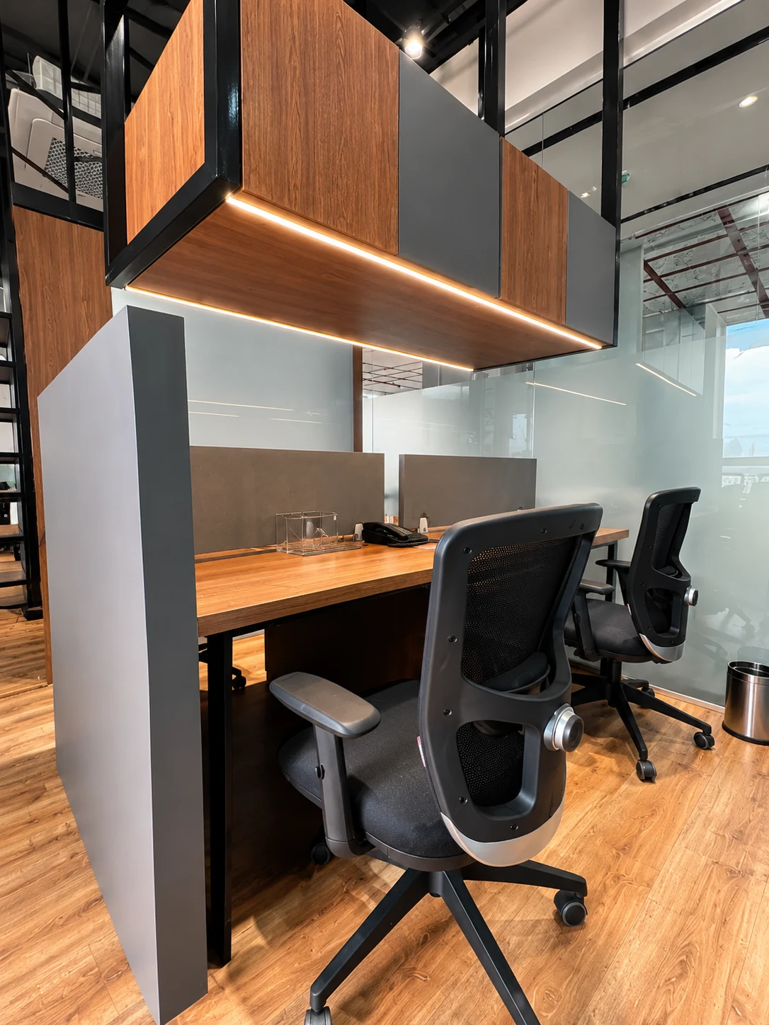 Desk area with dark chairs and a suspended wood-toned cabinet.