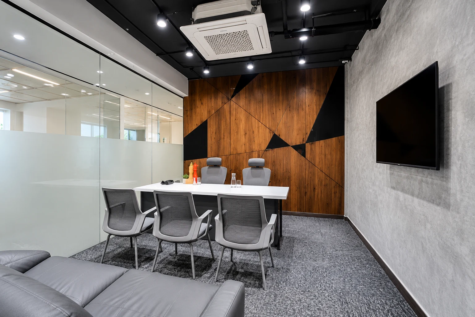 Meeting table and sofa beside frosted glazing and a geometric feature wall.