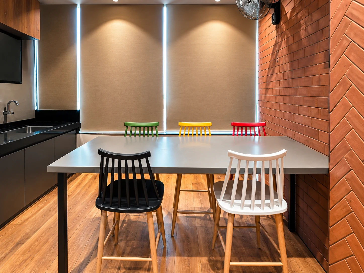 Shared pantry table with colourful chairs and a brick-patterned wall.